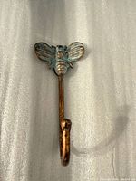 Front view of brass/bronze bee wall hook showing verdigris patina