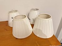 Four white pleated lamp shades grouped on tabletop, showing two wrapped and two unwrapped