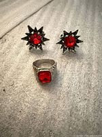 Front view of ring and starburst earrings showing red stones and silver-tone finish