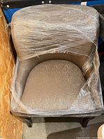 Front angled view of taupe barrel armchair wrapped in plastic
