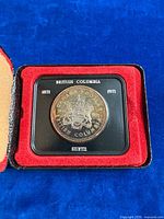 Coin seated in presentation case displaying reverse side and legend