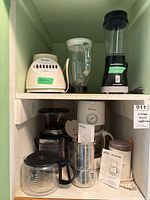 All countertop appliances arranged on two shelves: Osterizer blender, Hamilton Beach personal blender, Braun/Krups coffee maker, Braun/Krups coffee grinder, Toastmaster item, manuals and carafe visible.