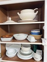Cabinet shelves showing Corelle plates, bowls, mugs, butter dish, wooden bowls and other pieces
