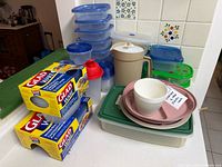 Counter with GladWare containers stacks, boxed sets, pitcher, shaker, plates