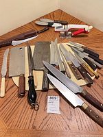 Full lot overview with all knives, cleaver, honing steel, manual sharpener, stone and cutting board displayed on table