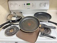 Overview of cookware on stove: two skillets, saucepan with lid, rectangular griddle