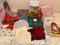 Group shot of all linens, napkins, aprons, oven mitts and placemat spread on bed