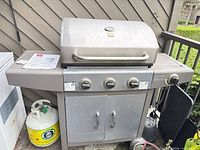 Front view of Terra Gear propane grill showing hood, control panel, cabinet doors, side shelves, propane tank beside unit