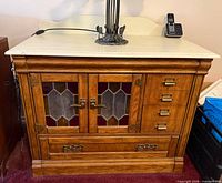 Front view of oak washstand cabinet showing marble-look top, stained-glass doors, drawers and brass hardware