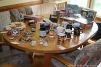 Full view of oval light wood table with round edges and extension leaf, surrounded by patterned chairs and various small household items on top (not included in sale).