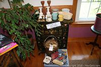 Metal ice bucket with lid and tongs on the floor in front of chest, assorted ceramic planters and candle holders on chest top