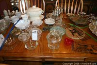 Full view of the table showing oval soup tureen, glass candy bowls with lids, chip and dip bowl, collapsible metal cup, and metal Asian wall plaques.