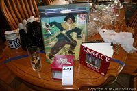 Photo showing Ken Scarecrow doll in original boxed packaging alongside Wizard of Oz book, ornament box and drinking glass.