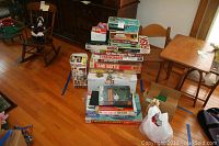 Overall view of vintage board games stacked on the floor, includes multiple boxed games and some building block sets