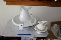 Large white ceramic pitcher and matching wash basin set, placed on a marble countertop, showing overall appearance and size comparison to smaller set.