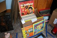 Wide image showing cardboard box of assorted vinyl records including Elvis Golden Records and Disney albums, along with a box containing more records and German language cassette course.