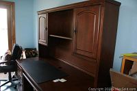 Front side view of wooden desk with hutch showing two cabinet doors on the top with an open shelf in between.