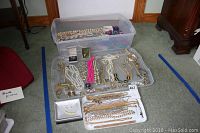Photo showing a large plastic bin holding various necklaces, bracelets, earrings, and beads along with trays displaying well arranged gold-tone chains, pearl necklaces, pink beads and pairs of earrings.