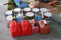 Overview of several paint cans arranged on floor with four plastic gas cans in front