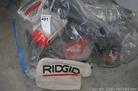 Ridgid miter saw and dust collection bag inside plastic packaging, showing the brand name 'Ridgid' on the bag and saw.