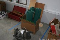 Photo showing the bench grinder placed on the floor near a box with green rolled foam mats inside.