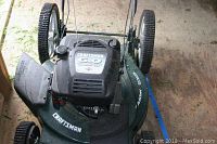 Top view of Craftsman 6.0 gas lawn mower showing black engine cover with brand and power specification, green mower deck, side discharge chute, and large rear wheels.