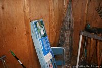 Photo showing boxed Porta Shade portable canopy leaning against wood wall with folding chair and tomato cages behind