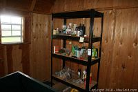 Photo showing black metal shelving unit in corner with various household chemicals on top shelves