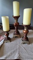 Front view of all three wooden candle holders with candles showing size gradation and metallic bases