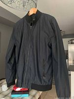 Front view of navy bomber jacket on hanger showing overall style, zipper closure and pocket