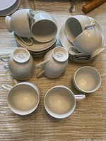 Top-down view showing multiple white cups and stacked saucers