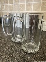 Both clear glass tankards side by side showing profile, handles and bases