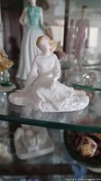 Seated Royal Doulton figurine on glass shelf