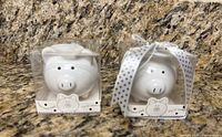 Two boxed white ceramic piggy banks side by side on countertop