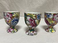 Front view of three hand-painted floral porcelain egg cups