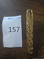 Gold Figaro chain coiled beside lot number slip