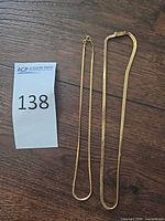 Two gold necklaces laid flat next to lot number tag