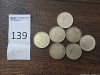 Seven Morgan silver dollars arranged on wooden surface next to lot number slip