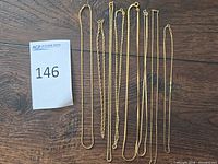 Group shot of all eight 14KT gold necklaces on wood surface with lot tag