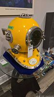 Full view of yellow diving helmet on glass table showing overall form, color and fittings