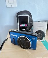 Blue Canon PowerShot SX270 HS and silver Canon camera with case on tabletop