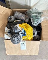 Open box showing several black sprinkler bodies, bag of green drip emitters, additional fittings and instruction leaflet