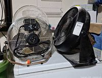 Two floor fans: metal cage fan and black plastic circulator fan on appliance top
