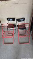 Front view of all four folding chairs: two red wire chairs, two black plastic chairs