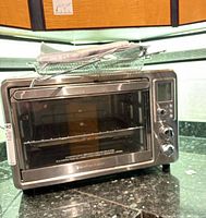 Front view of Hamilton Beach stainless steel toaster oven with mesh basket and manual on top