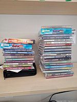 Two stacks of karaoke CD+G jewel cases and black carrying pouch on shelf