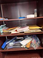 Overall view of shelves containing stapler, hole punch, envelopes, notebooks, clips bagged, power strip