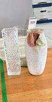 Three vases on floor: textured glass, green-tint cylinder, ceramic with flower