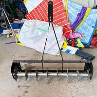 Front view of the spike aerator showing frame, hitch arm, shaft and spike wheels