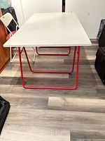 Full view of white laminate folding table with red metal folding legs